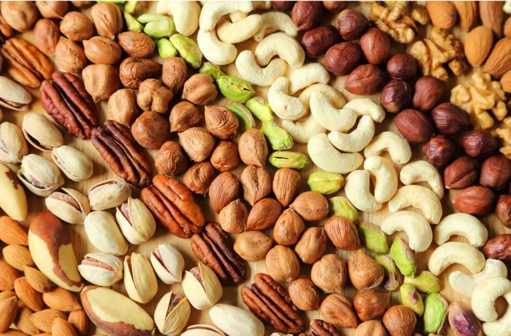 Assorted nuts in a rustic bowl, including almonds, walnuts, hazelnuts, and cashews, on a wooden table.