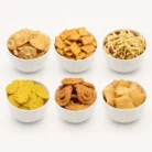 Diwali Indian savoury snacks festive collection featuring six varieties of traditional golden-brown Indian namkeen served in white bowls.